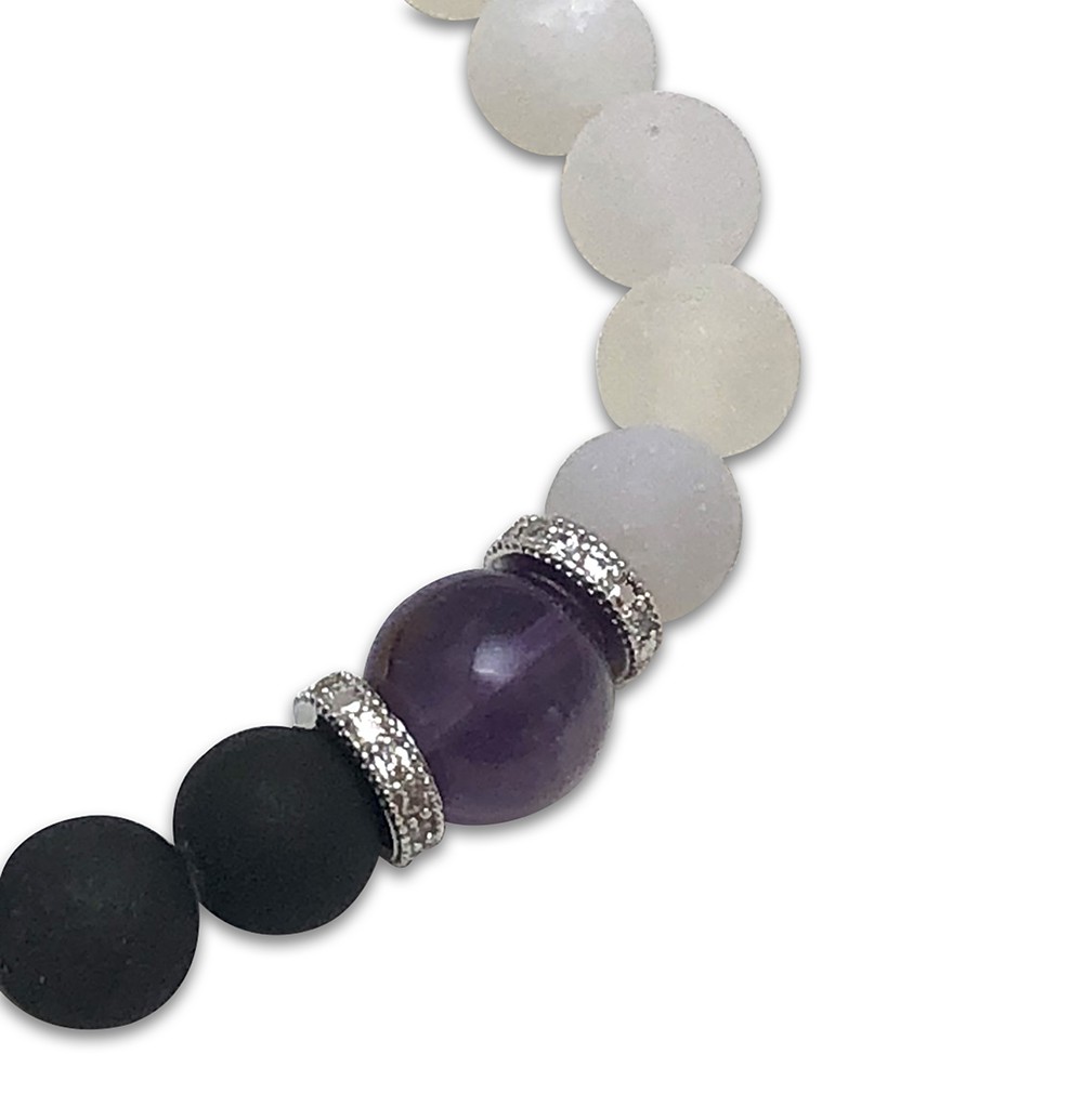 A close-up of a beaded bracelet with black, white, and a single purple bead.