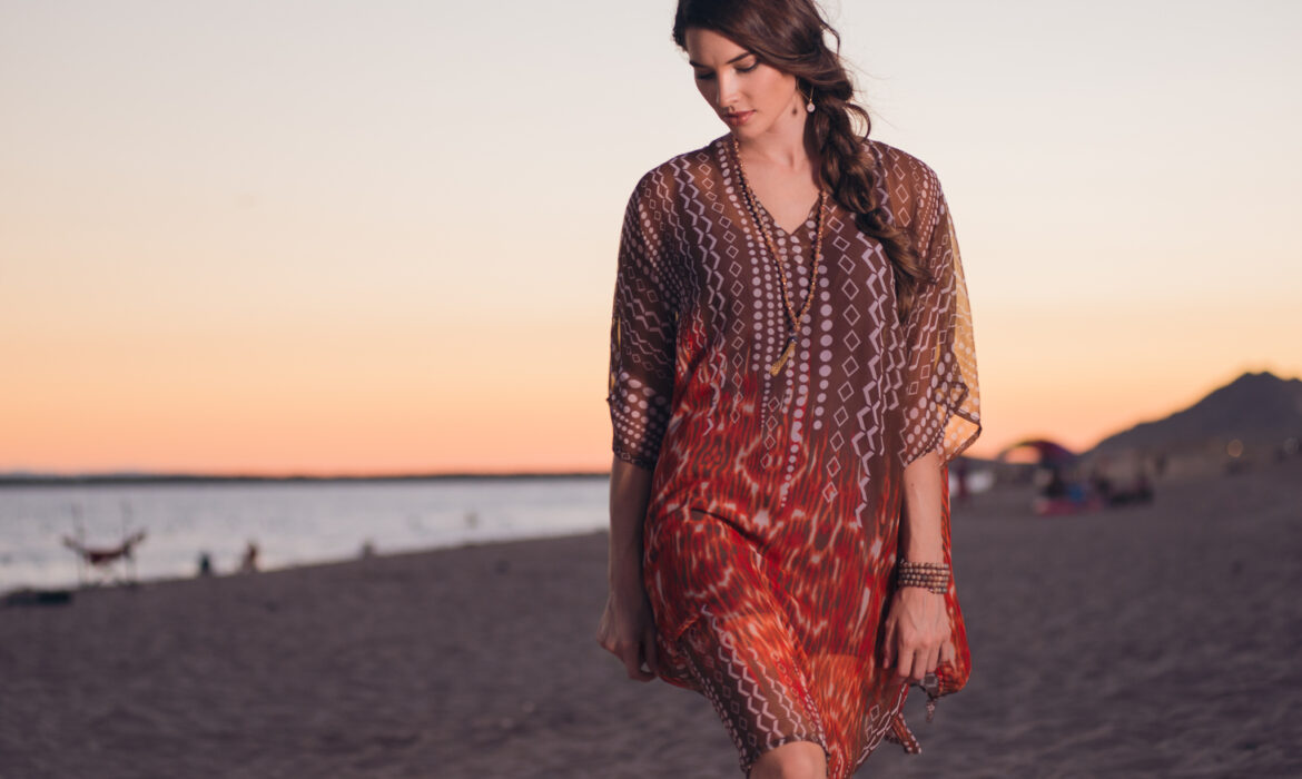 Woman in a patterned dress standing on the beach at sunset.